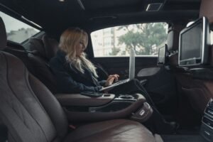A businesswoman working on a laptop inside a luxury car, showcasing professionalism and modern technology.